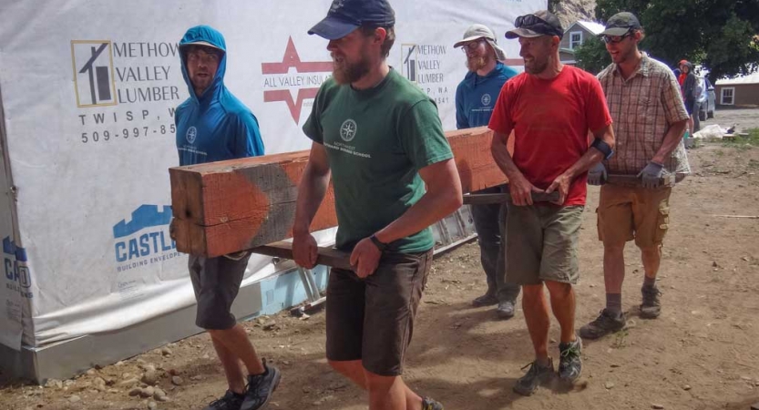 a group of veterans carry a large piece of wood during a service project
